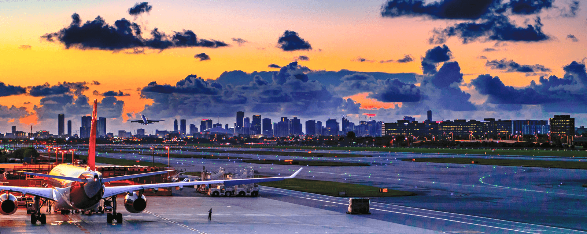 Airplanes on the tarmac at Miami International Airport at sunset, downtown skyline in the distance