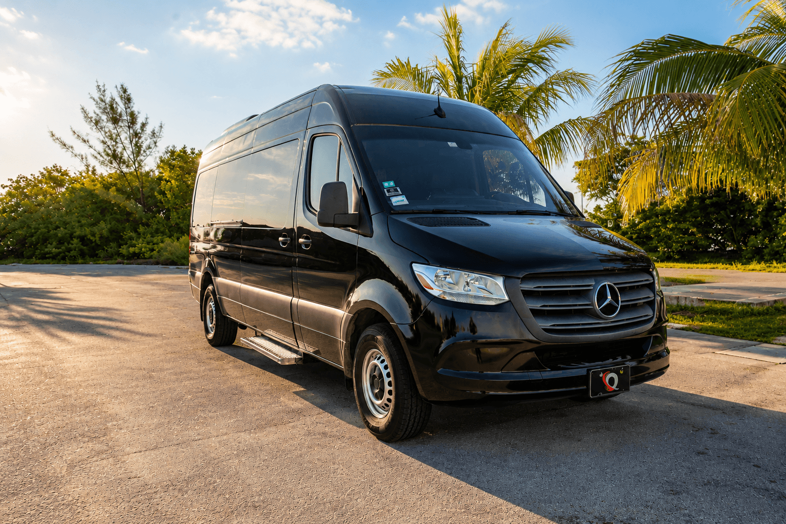 An Miami Bus Company Sprinter van parked under palm trees at golden hour, front three-quarter angle